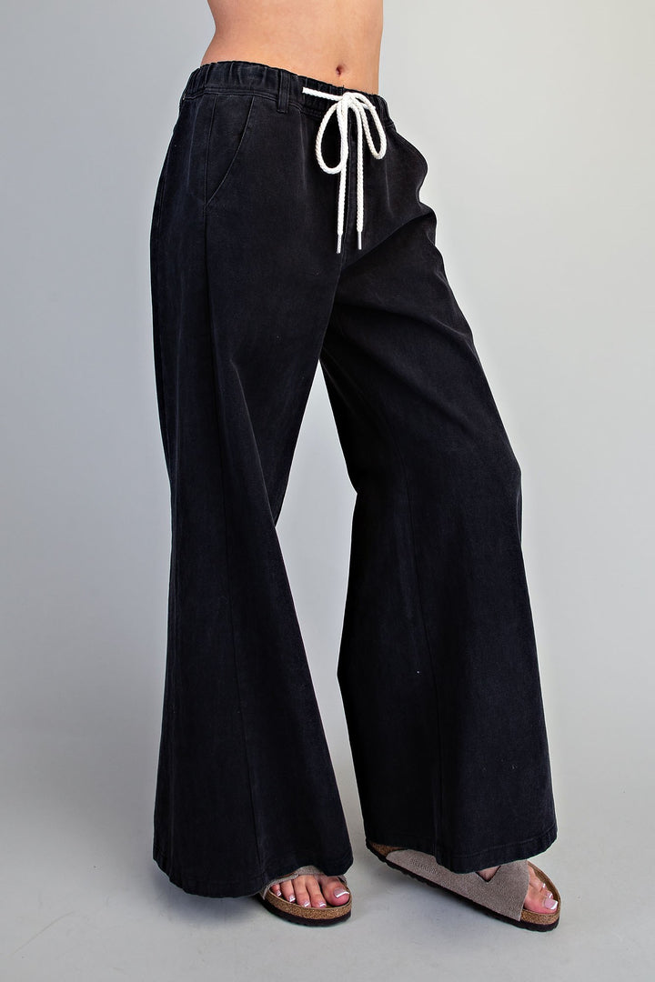 Black wide-leg pants with a white drawstring waist, shown on a model from the waist down against a light gray studio background.