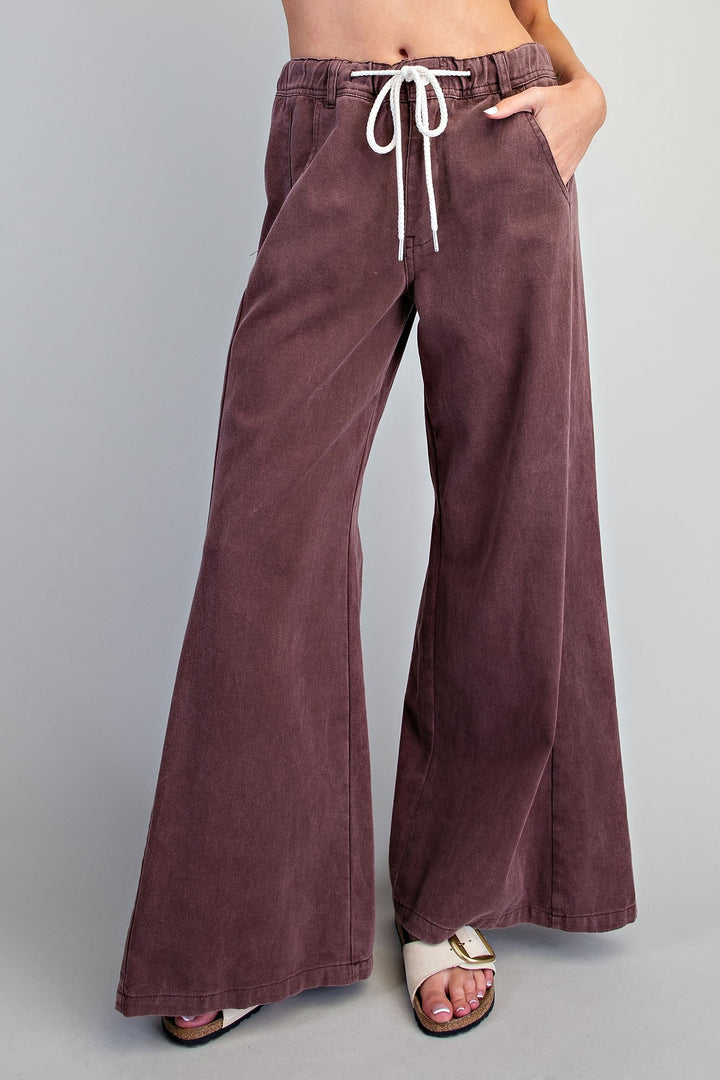 A person wearing wide-leg corduroy pants in a muted mauve-brown color with a white drawstring, paired with white slide sandals, against a solid gray studio background.