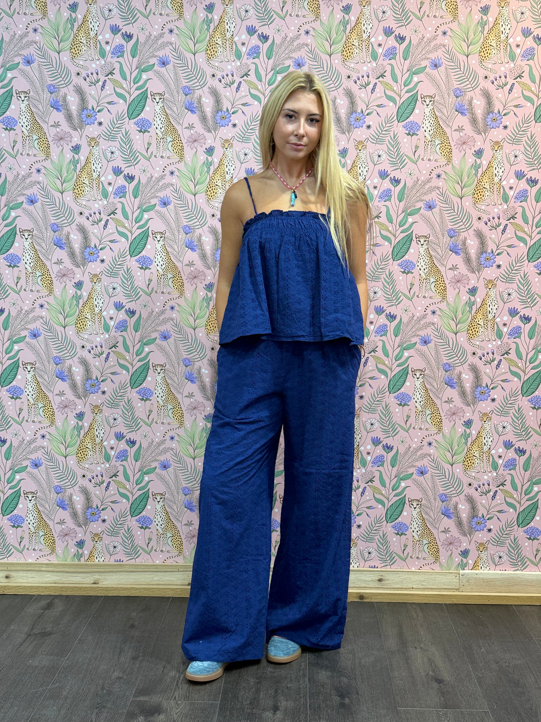 Woman wearing a blue outfit standing against a patterned wall.