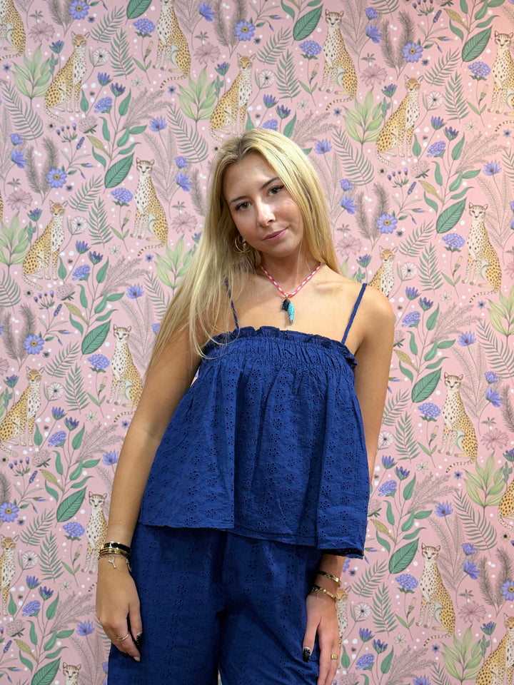 Woman wearing a blue top and pants against a patterned wall with animals and plants.