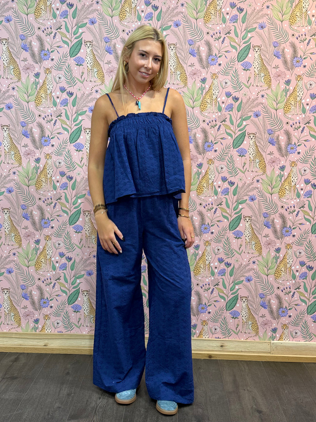 Woman wearing a blue jumpsuit standing in front of a patterned wall.