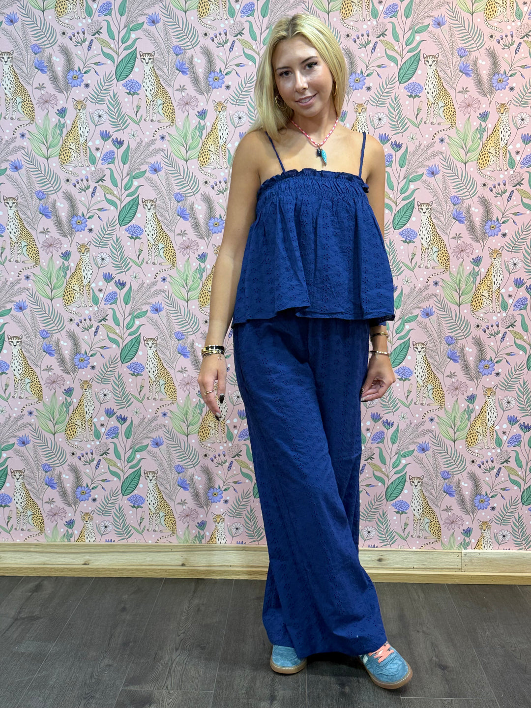 Woman wearing a blue top and pants standing against a patterned wall.