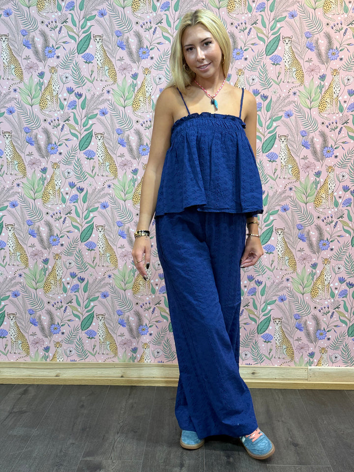 Woman wearing a blue top and pants standing against a patterned wall.
