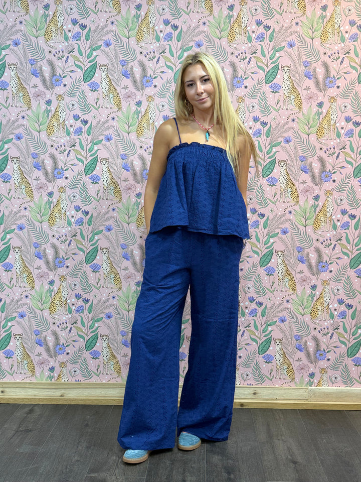 Woman wearing a blue outfit standing against a decorative wallpapered wall.