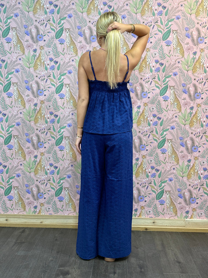 Woman wearing a blue jumpsuit standing against a floral wallpapered wall.