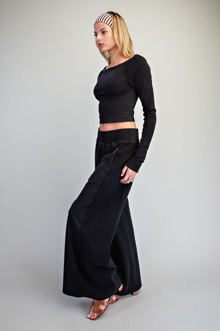 A woman modeling a black two-piece outfit consisting of a long-sleeve cropped top and matching wide-leg pants, paired with a black and white striped headband, against a plain light gray studio background.