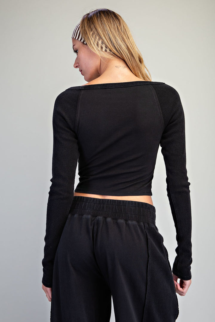 A woman shown from the back wearing a black long-sleeve crop top with raglan sleeves and black sweatpants against a plain light gray studio background.