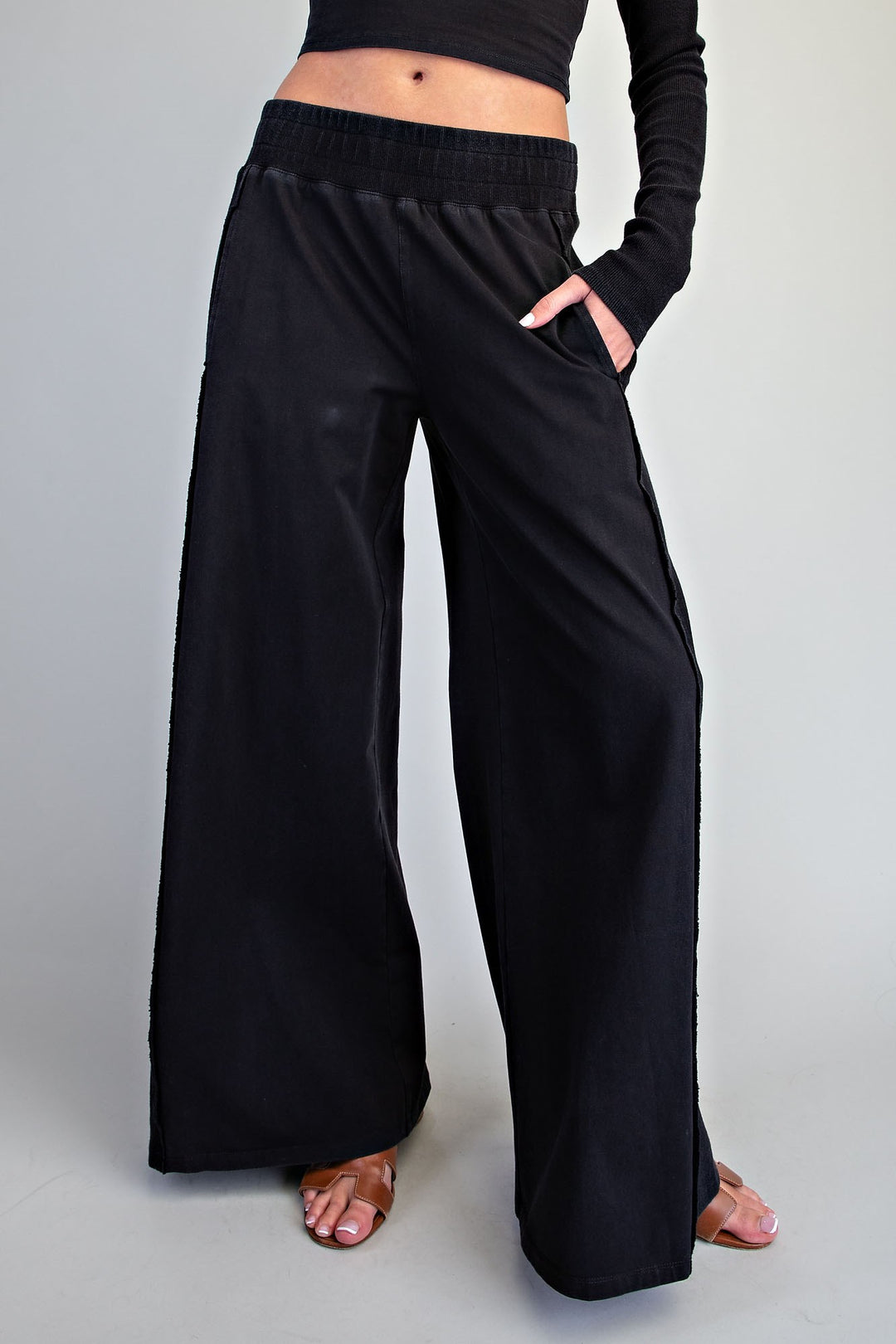 Black wide-leg lounge pants with an elastic waistband and side pockets, shown on a model from the waist down against a light gray studio background.