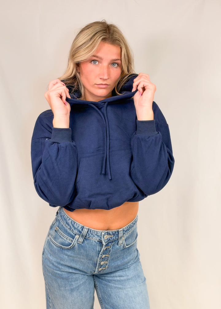 Woman wearing cropped blue hooded sweatshirt with jeans on plain background
