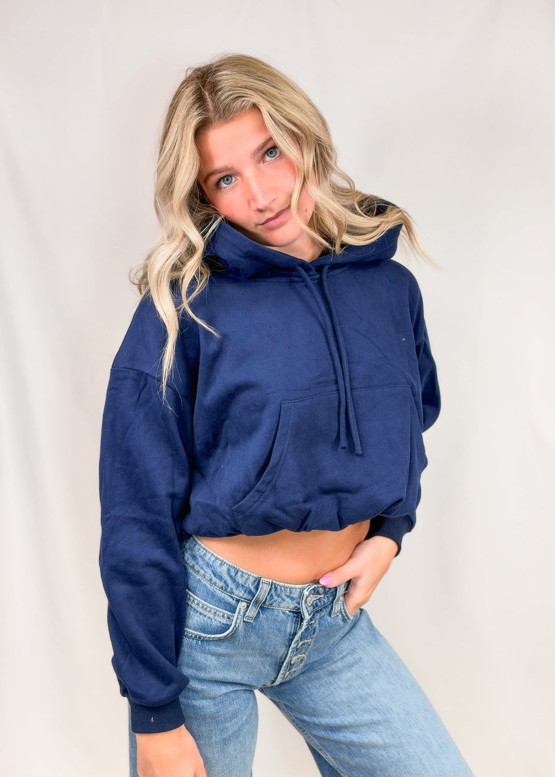 Woman wearing blue cropped hooded sweatshirt with jeans on plain background