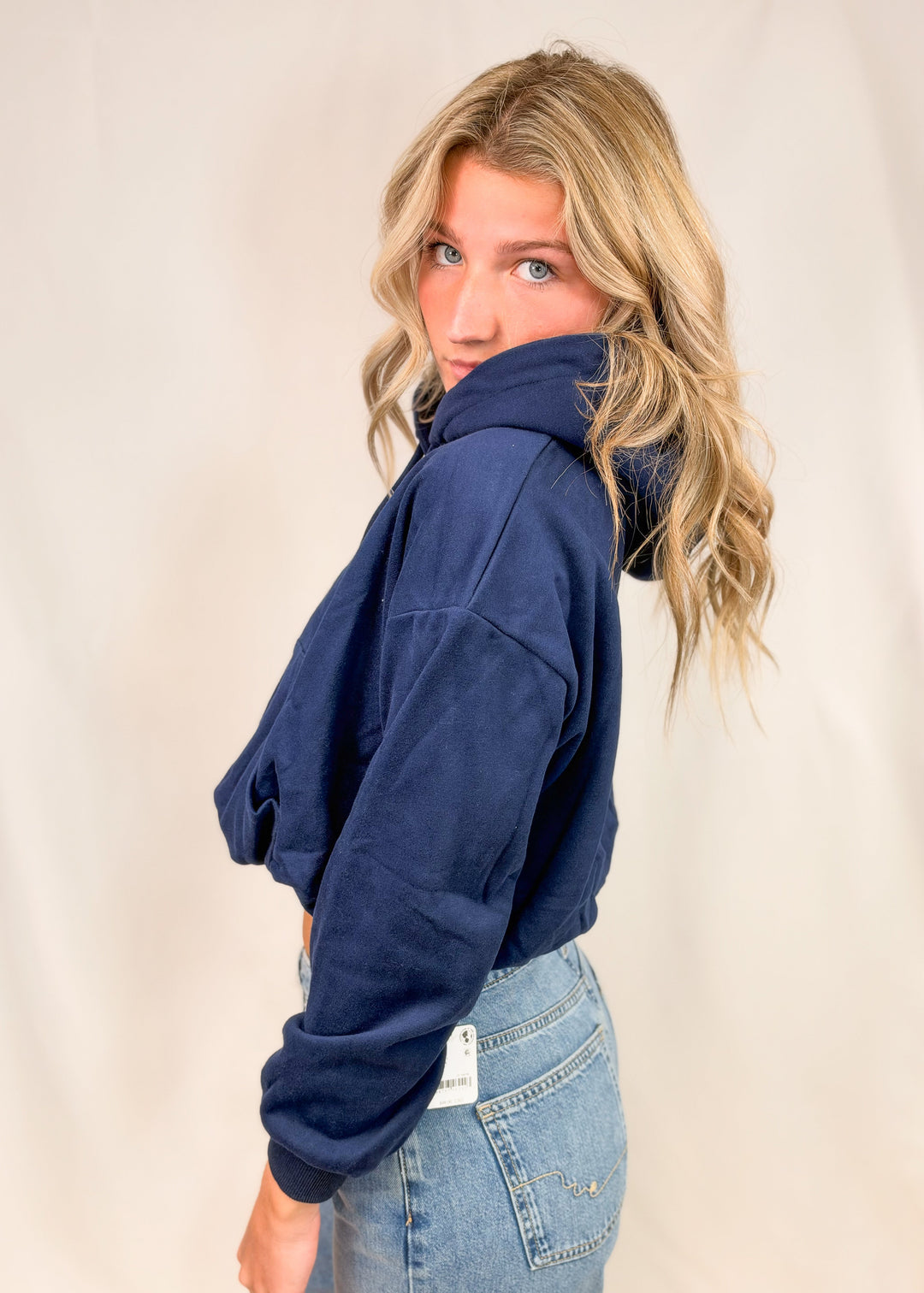 Woman shown from side view wearing blue hooded sweatshirt and jeans on plain background