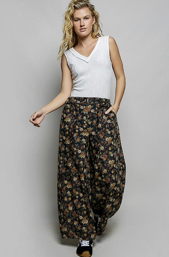 A woman modeling a sleeveless white top and wide-leg floral pants against a light gray studio background.