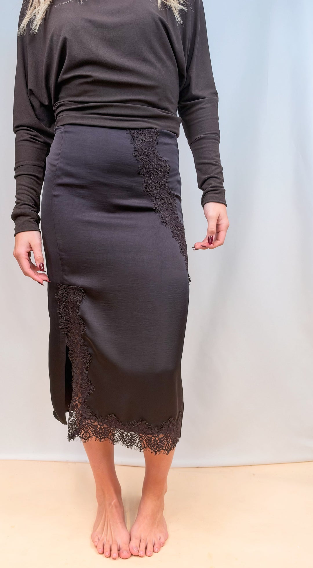 Woman wearing brown long sleeve top and brown satin skirt on plain background