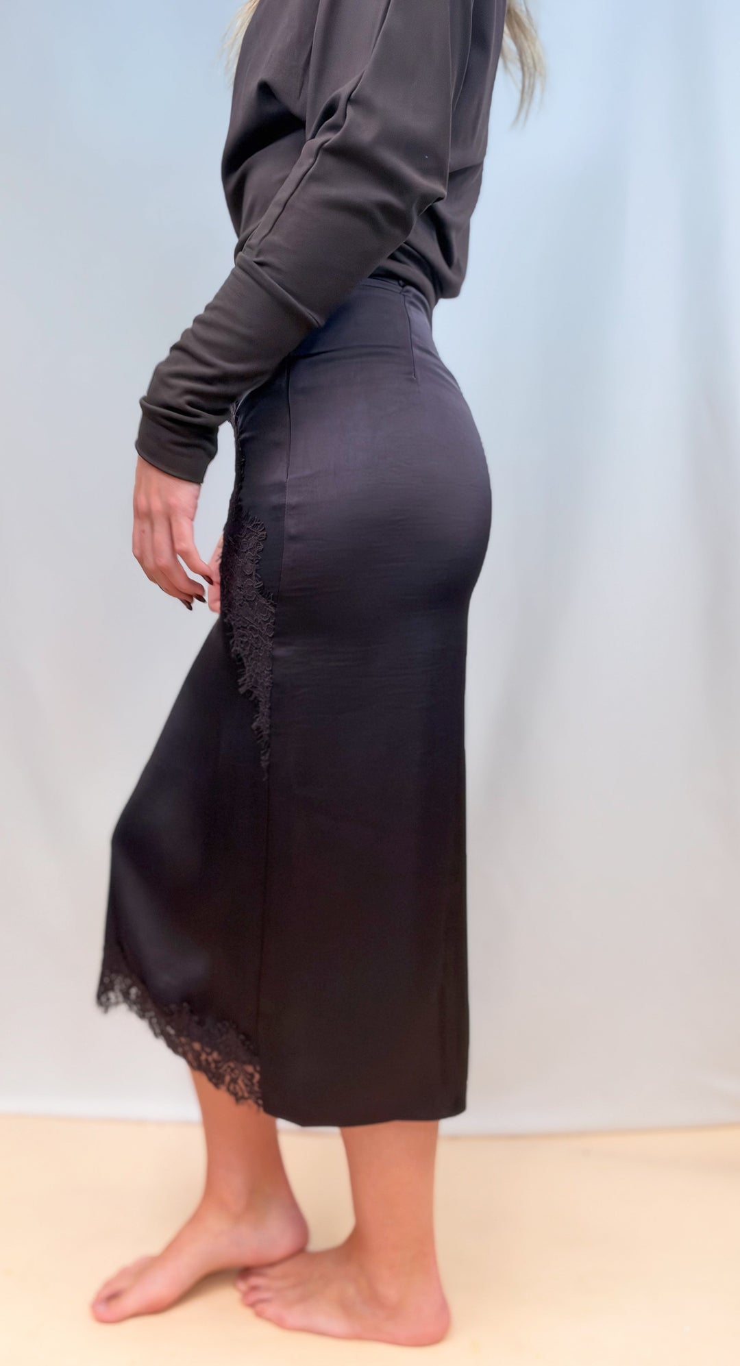 Woman shown from side view wearing brown long sleeve top with brown satin skirt on plain background