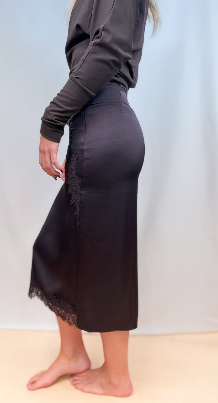 Woman shown from side view wearing brown long sleeve top with brown satin skirt on plain background