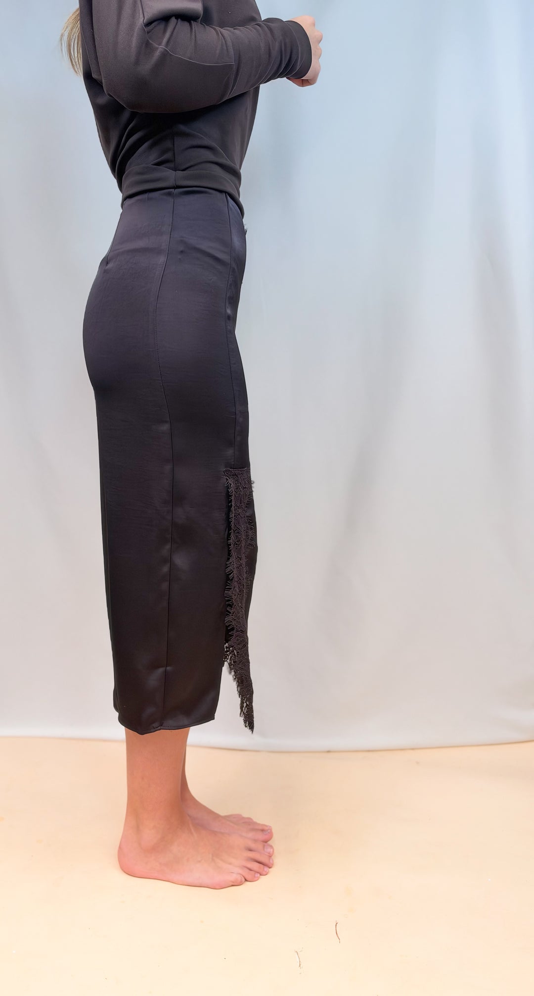 Woman shown from side view wearing brown long sleeve top and brown satin skirt on plain background