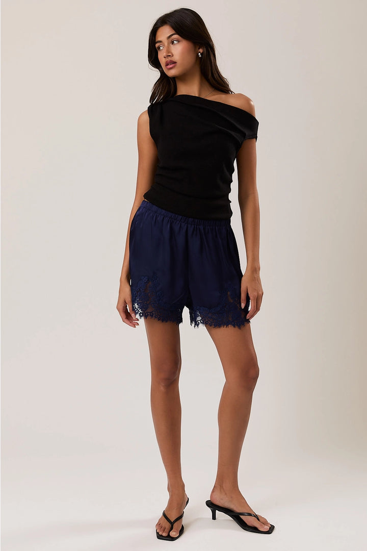 Woman wearing navy satin shorts with lace trim and black top on plain background