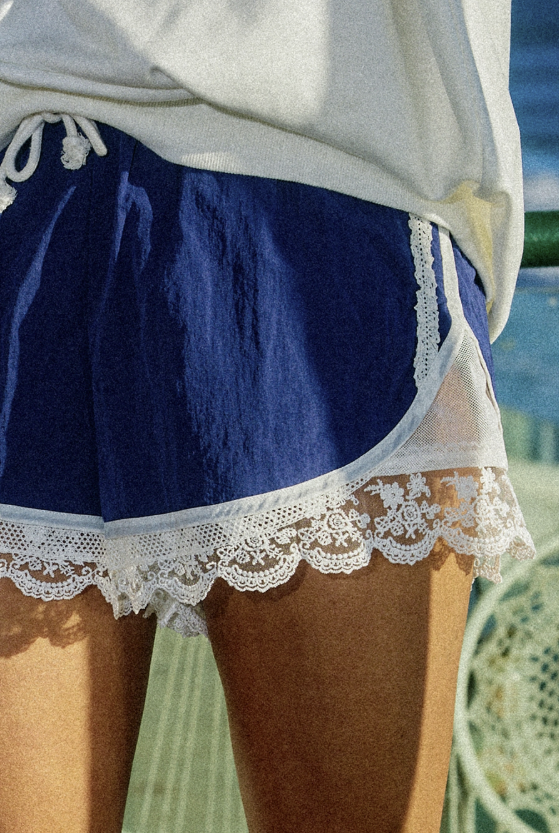 Navy blue shorts with lace trim worn over a white garment, against a blurred natural background.