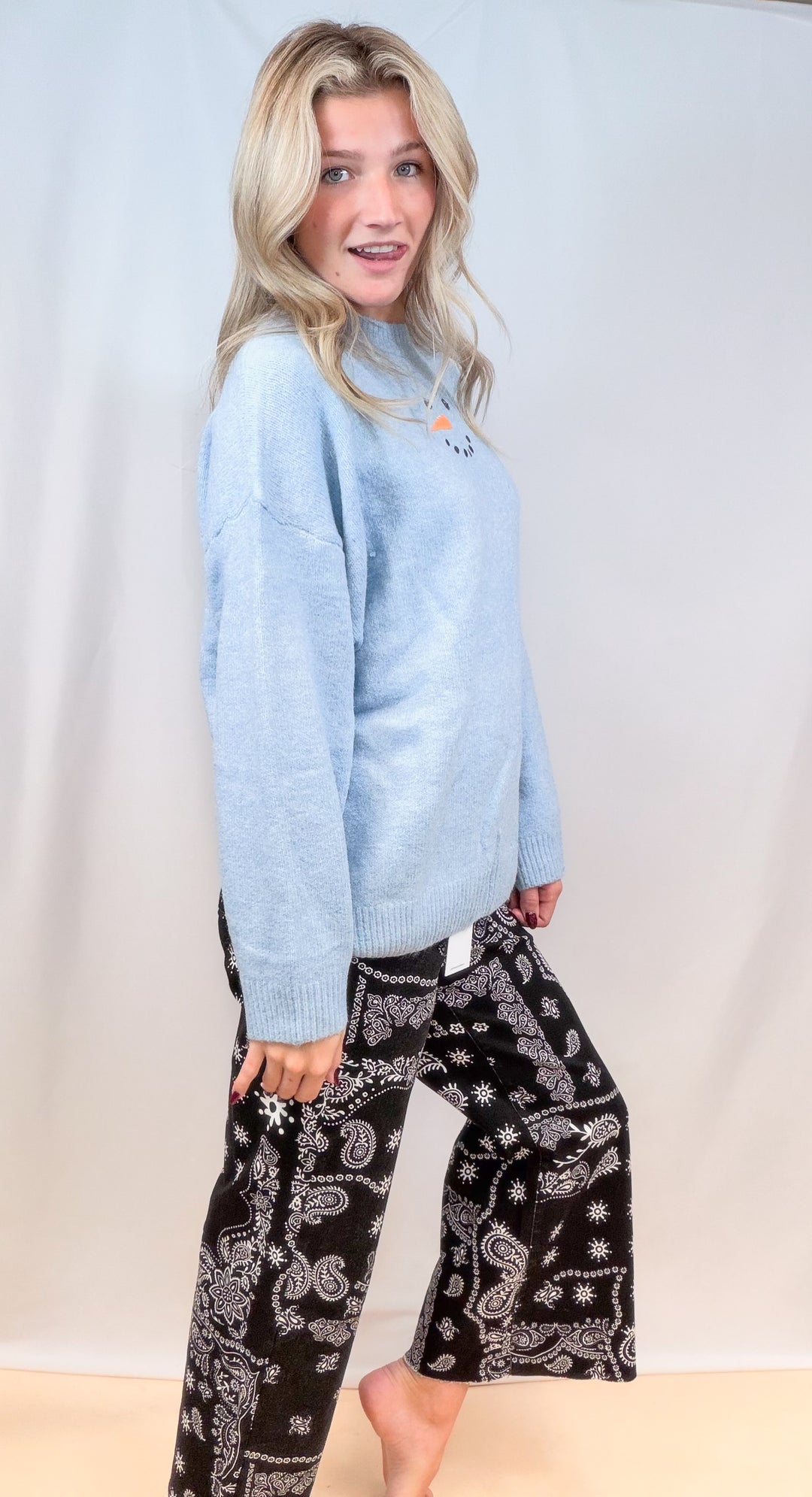 Woman shown from side view wearing light blue sweater with black bandana pants on plain background