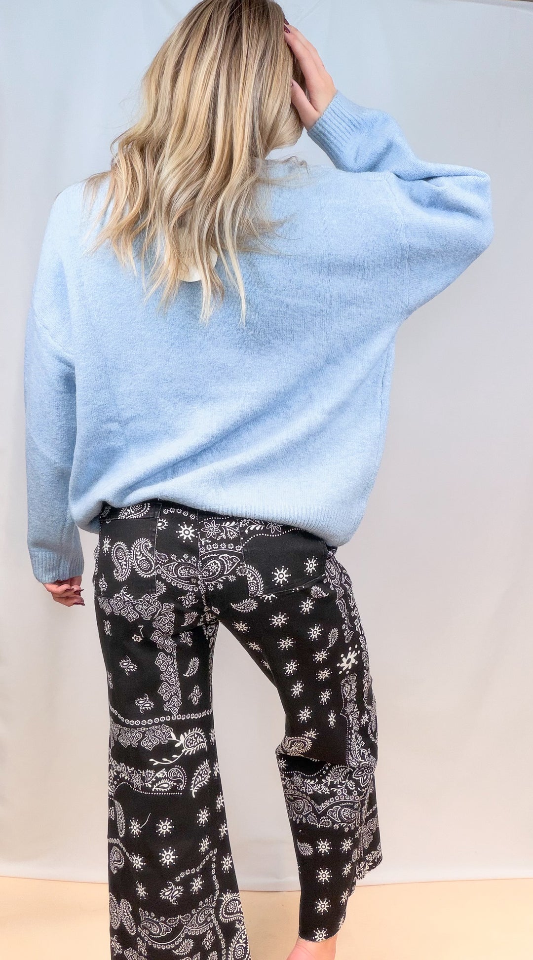 Woman shown from back view wearing light blue sweater and black bandana pants on plain background