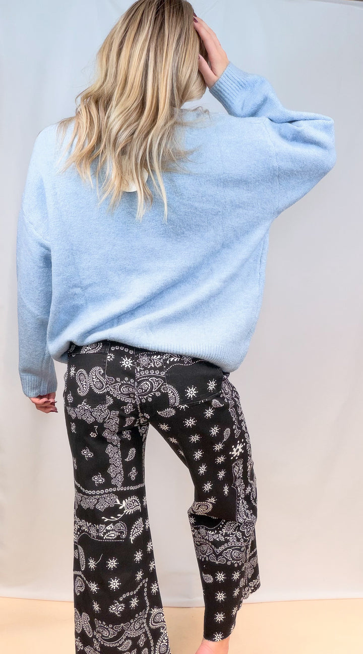 Woman shown from back view wearing light blue sweater and black bandana pants on plain background