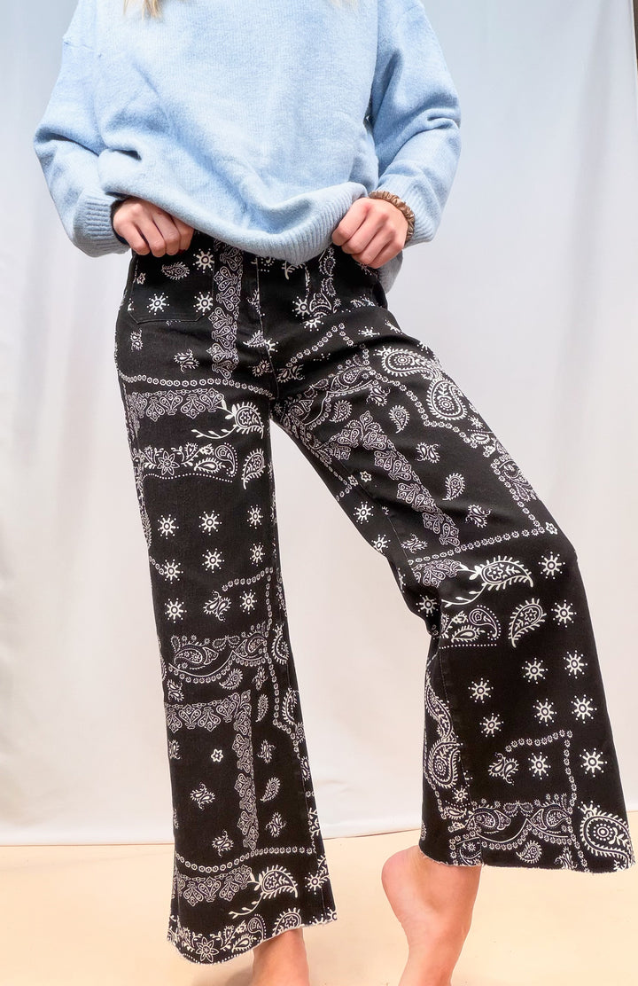 Woman shown from waist down wearing black bandana pants on plain background