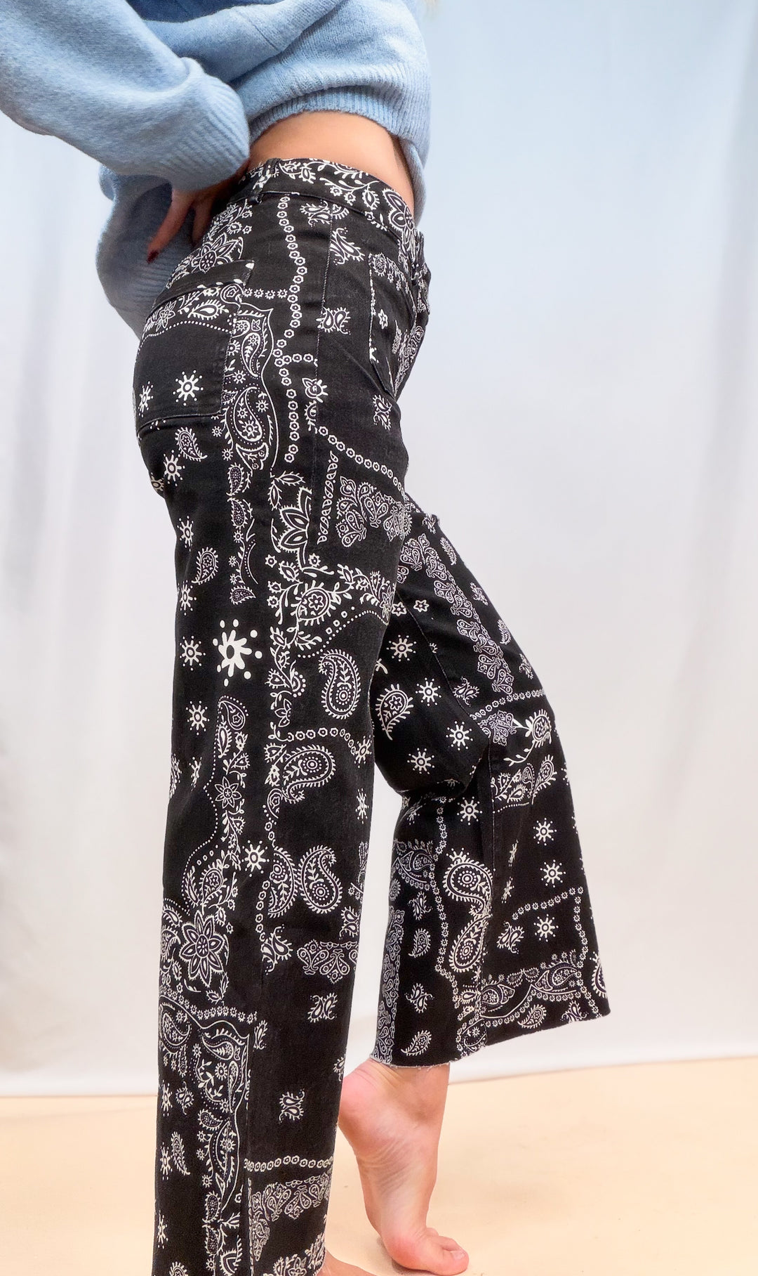 Woman shown from side view waist down wearing black bandana pants on plain background