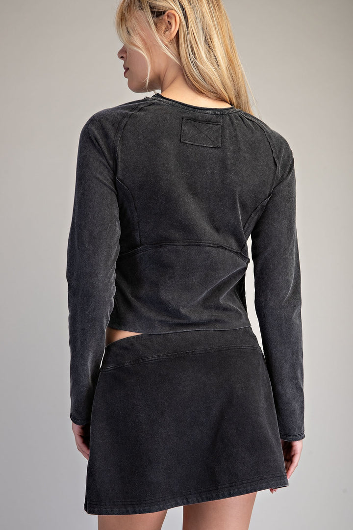 A woman shown from the back wearing a dark washed charcoal long-sleeve crop top and matching mini skirt set against a plain light gray studio background.