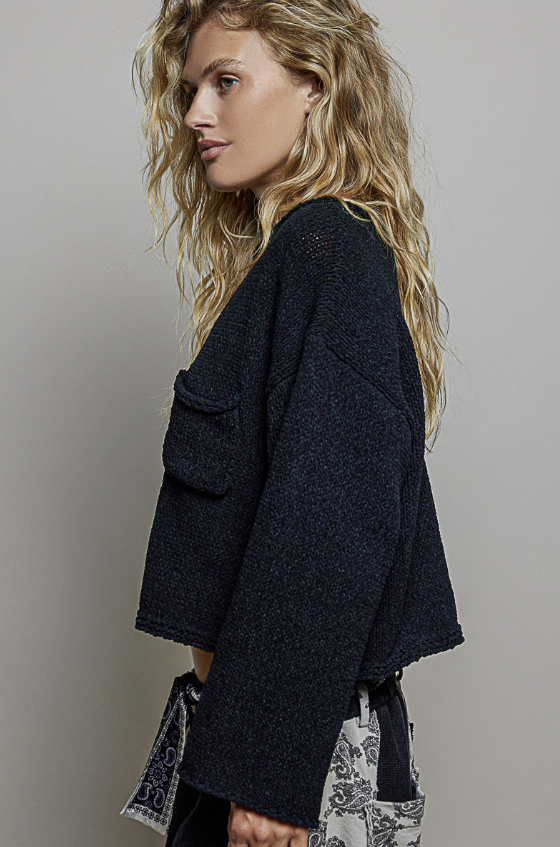 A woman wearing a dark navy blue textured knit cropped jacket with large front patch pockets, shown in a side profile against a plain light gray studio background.