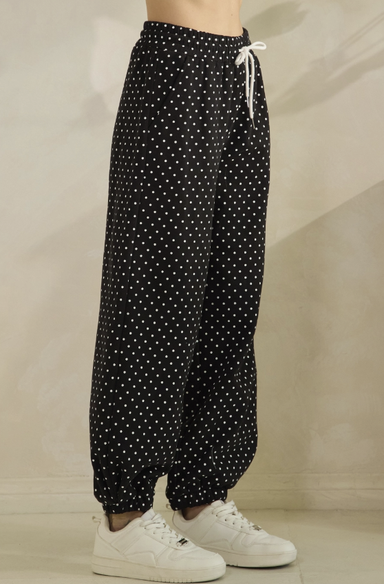 Black wide-leg harem pants with a white polka dot pattern, featuring a white drawstring waist and elastic cuffs, modeled with white sneakers.