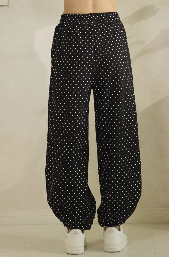 Black wide-leg pants with a white polka dot pattern, shown on a model from the waist down wearing white sneakers.