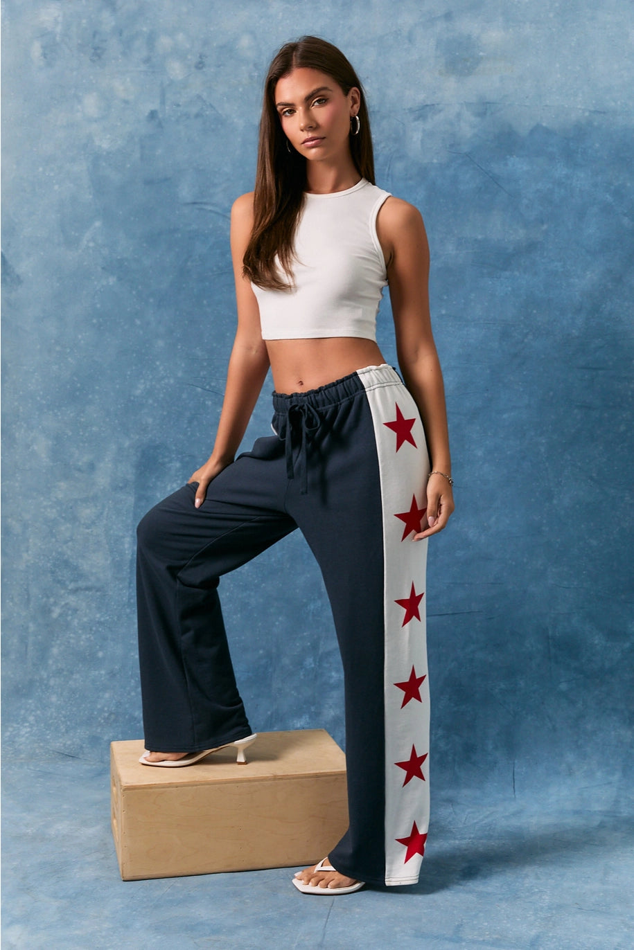 Woman wearing a white top and dark pants with red star patterns on a blue background