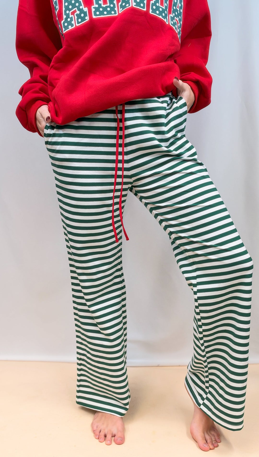 Woman shown from waist down wearing green and white stripe pants on plain background