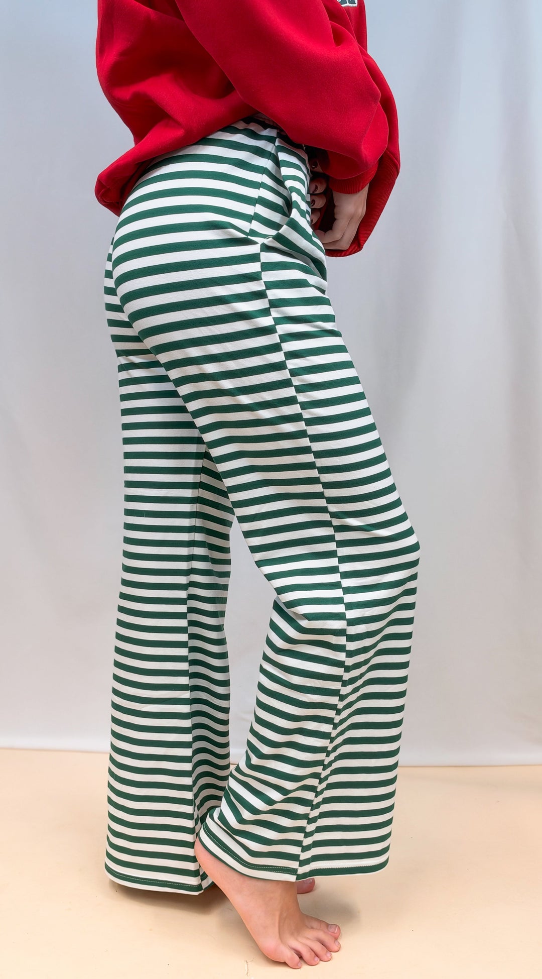 Woman shown from side view from waist down wearing green and white stripe pants on plain background