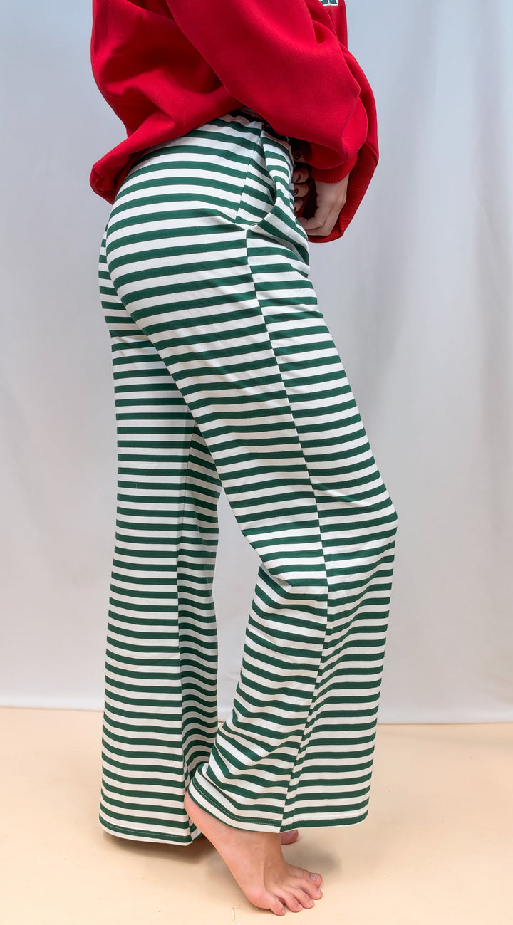 Woman shown from side view from waist down wearing green and white stripe pants on plain background