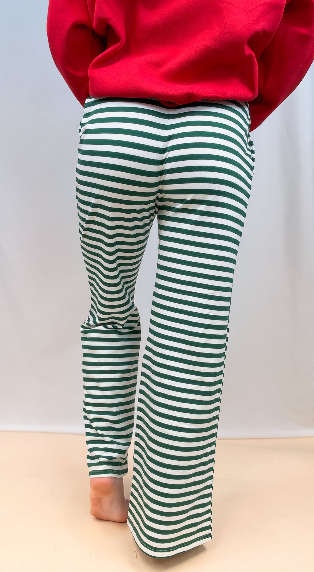 Woman shown from back view waist down wearing green and white stripe pants on plain background