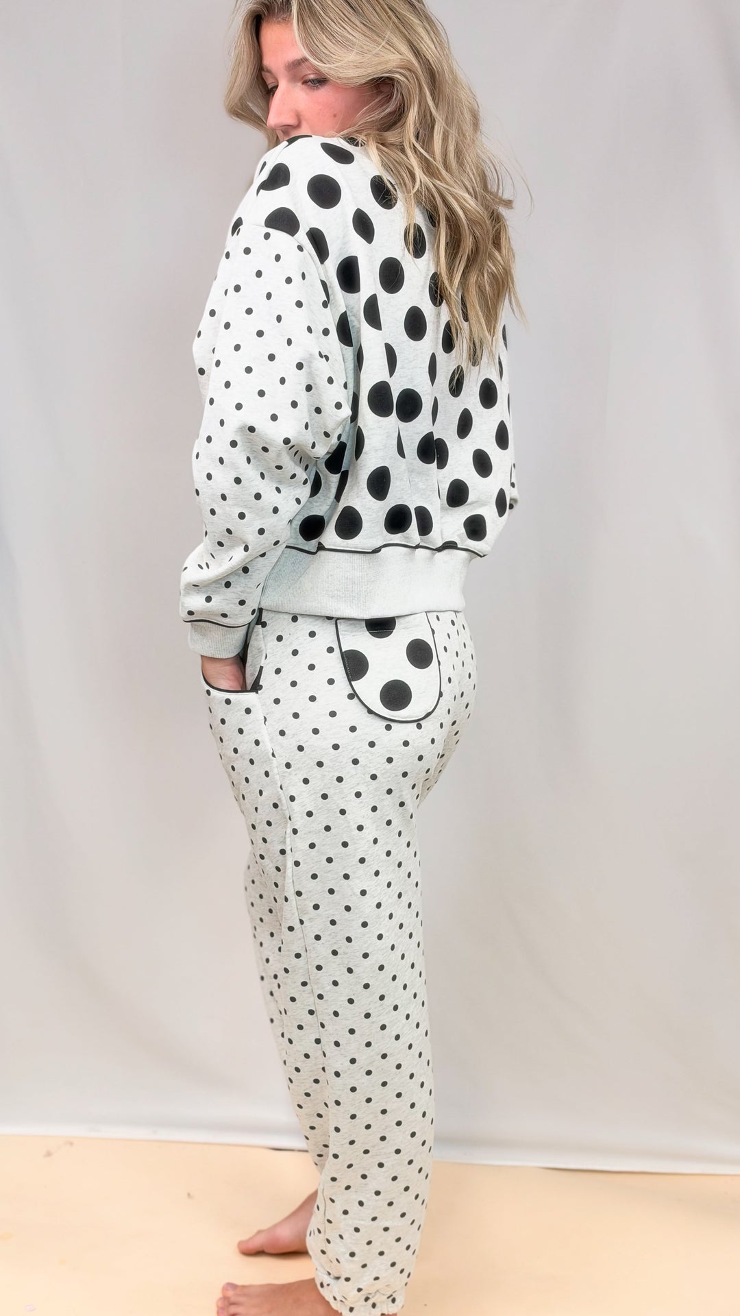 Woman shown from side wearing grey matching sweatsuit with black polka dots on top and bottom on plain background