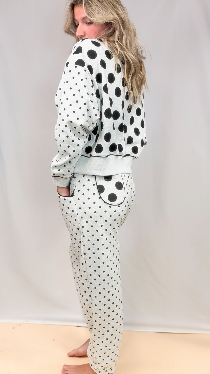 Woman shown from side wearing grey matching sweatsuit with black polka dots on top and bottom on plain background