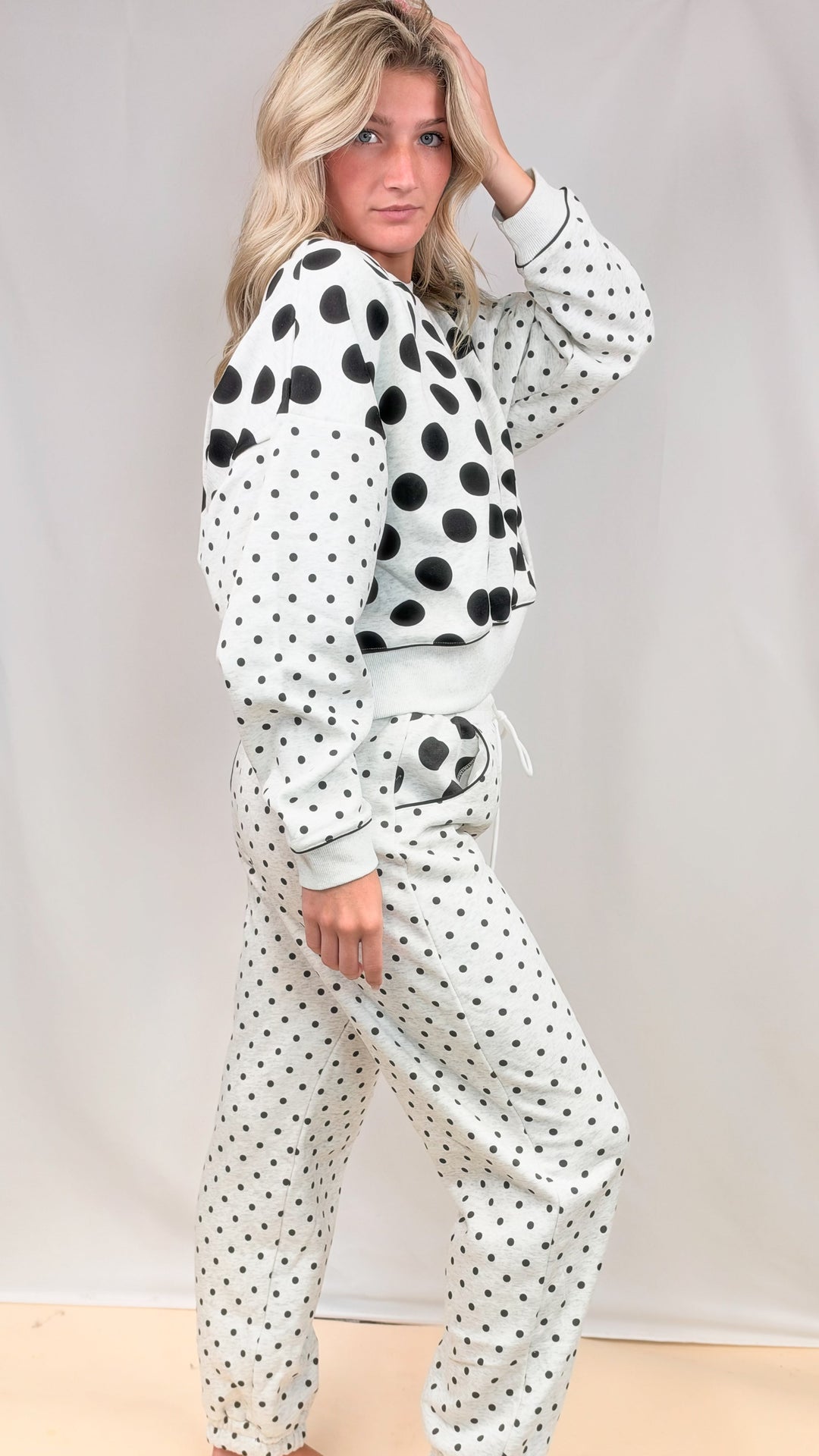 Woman wearing grey matching sweatsuit with polka dots on top and bottom on plain background