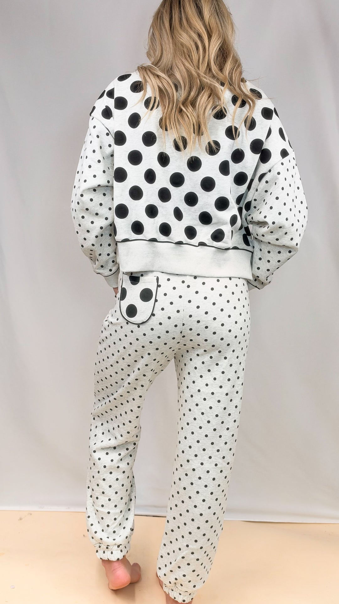 Woman shown from back wearing grey matching sweatsuit with polka dots on plain background