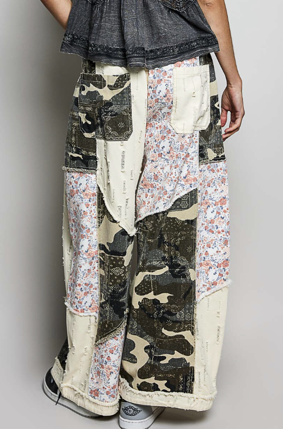 Person wearing patchwork pants with camouflage and floral patterns on a plain background