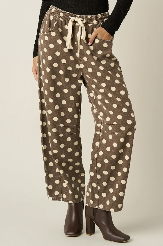 Brown wide-leg pants with a cream polka dot pattern, featuring an elastic drawstring waistband and side pockets, modeled with a black top and brown leather ankle boots.