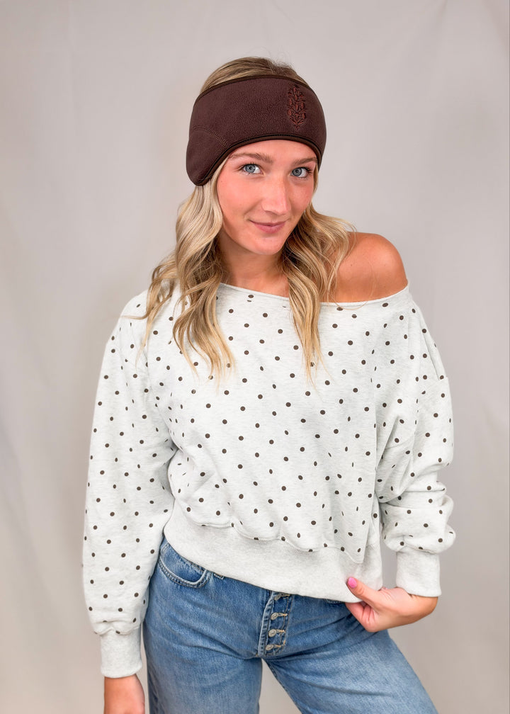 Woman wearing heather grey sweatshirt with brown polka dots and jeans on plain background