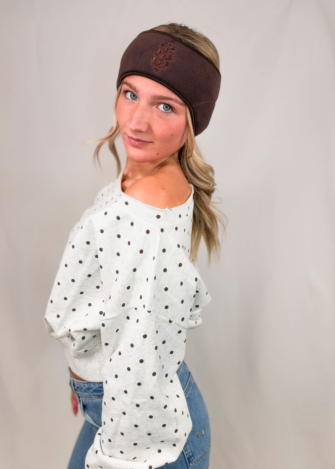 Woman wearing heather grey off shoulder sweatshirt with brown polka dots on plain background