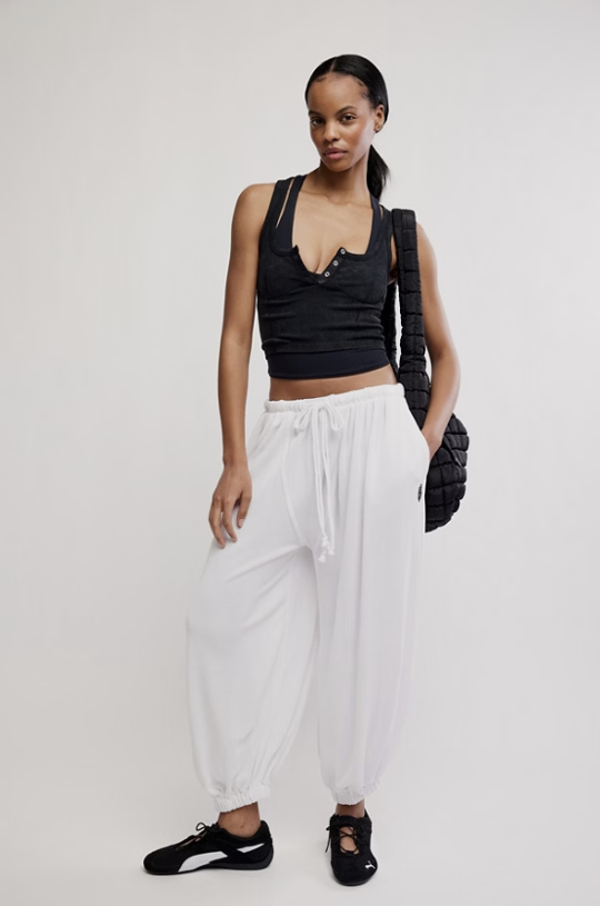 Woman wearing a black tank top and white pants with a black bag on a white background