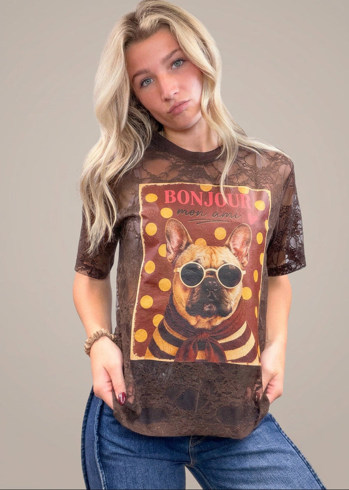 Woman wearing brown lace tee with french bulldog graphic on front with denim jeans on plain background