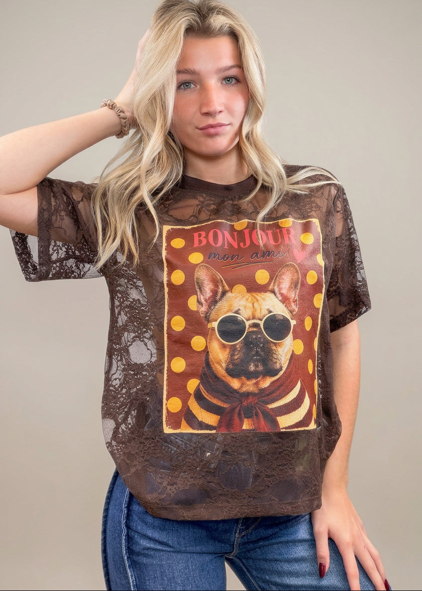 Woman wearing brown lace tee with french bulldog graphic on front with denim jeans on plain background