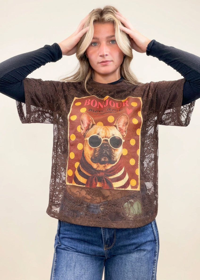 Woman wearing brown lace tee with black long sleeve under. Brown lace tee has french bulldog graphic on front worn with denim jeans on plain background