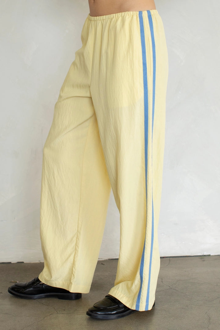 Yellow pants with blue stripes worn by a person against a white wall.