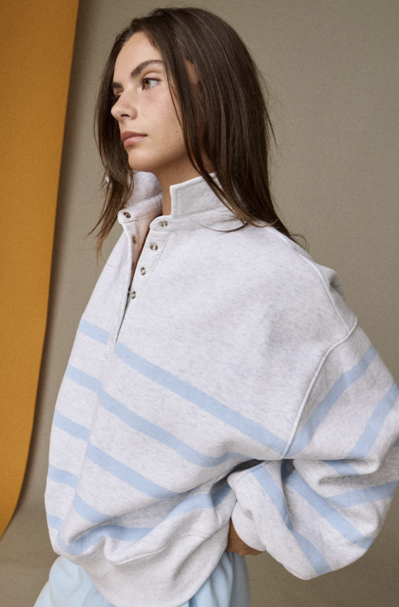 Woman wearing heather grey and light blue stripe pullover on plain background